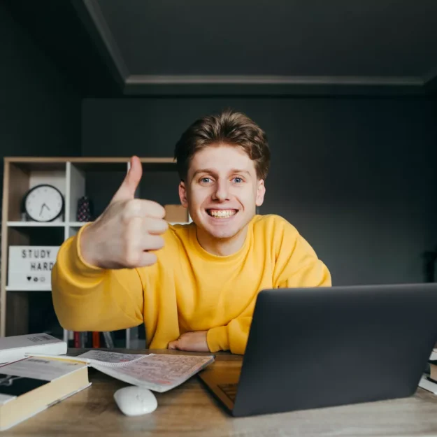 Young person giving thumbs up whilst sat at desk